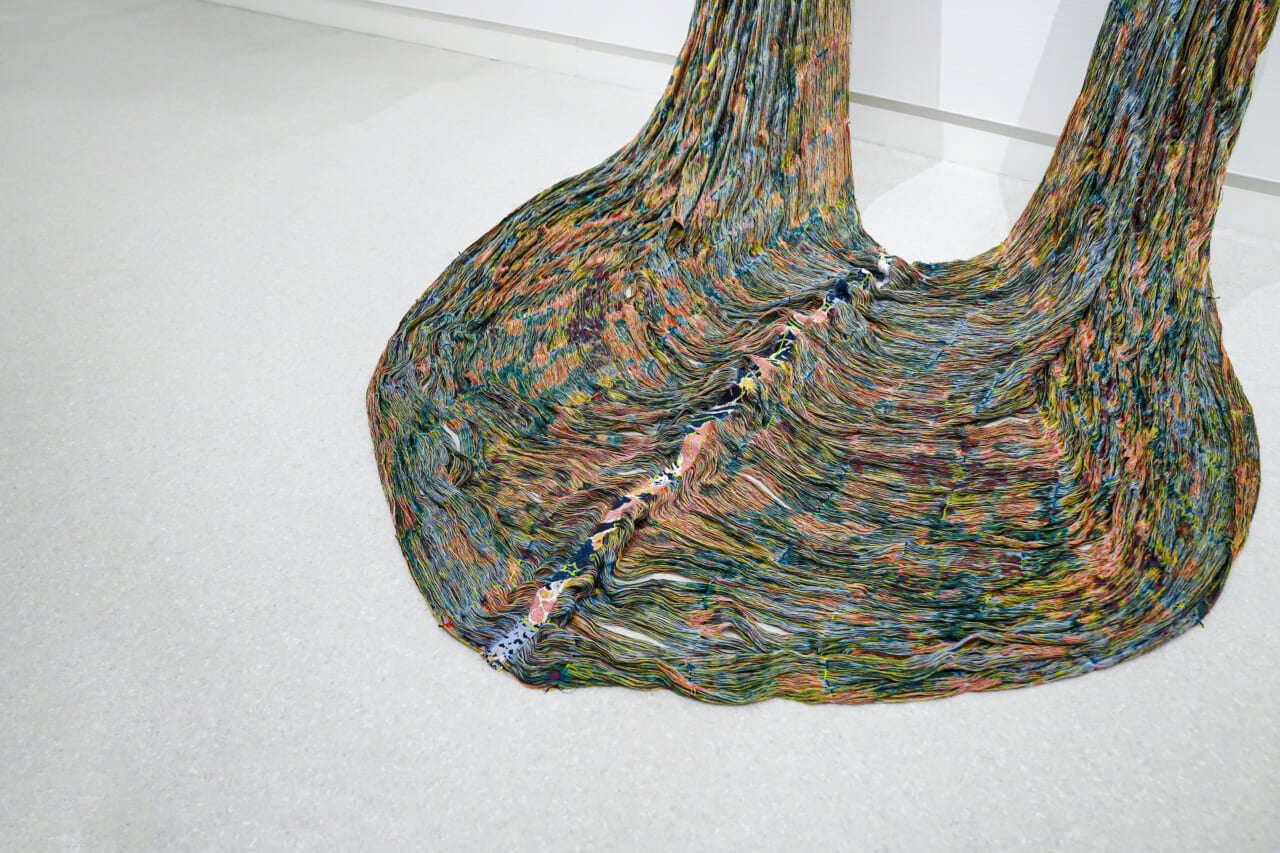 手塚愛子《Certainty / Entropy（Japan 2-2）》（部分）2016　手塚愛子さんから作品のご説明をいただきました。「この織物は作家自身のデザインにより、8世紀の『紺地花樹双鳥文きょうけち』（正倉院蔵）を引用して織られています。その古代の染物の模様の中に、現代を生きる私たちを取り巻くさまざまなシンボルが散りばめられ、それ自体が装飾の一部として存在しています。その現代のシンボルとは、コピーライトマーク、@マーク、原発のマーク、ピースマーク、クレジットカード会社のシンボル、遺伝子のイメージ、放射線照射済みマーク、子宮のイメージ、バイオハザードマーク、などです。これらのシンボルが、古代の文様の中に見え隠れし、共存しています」